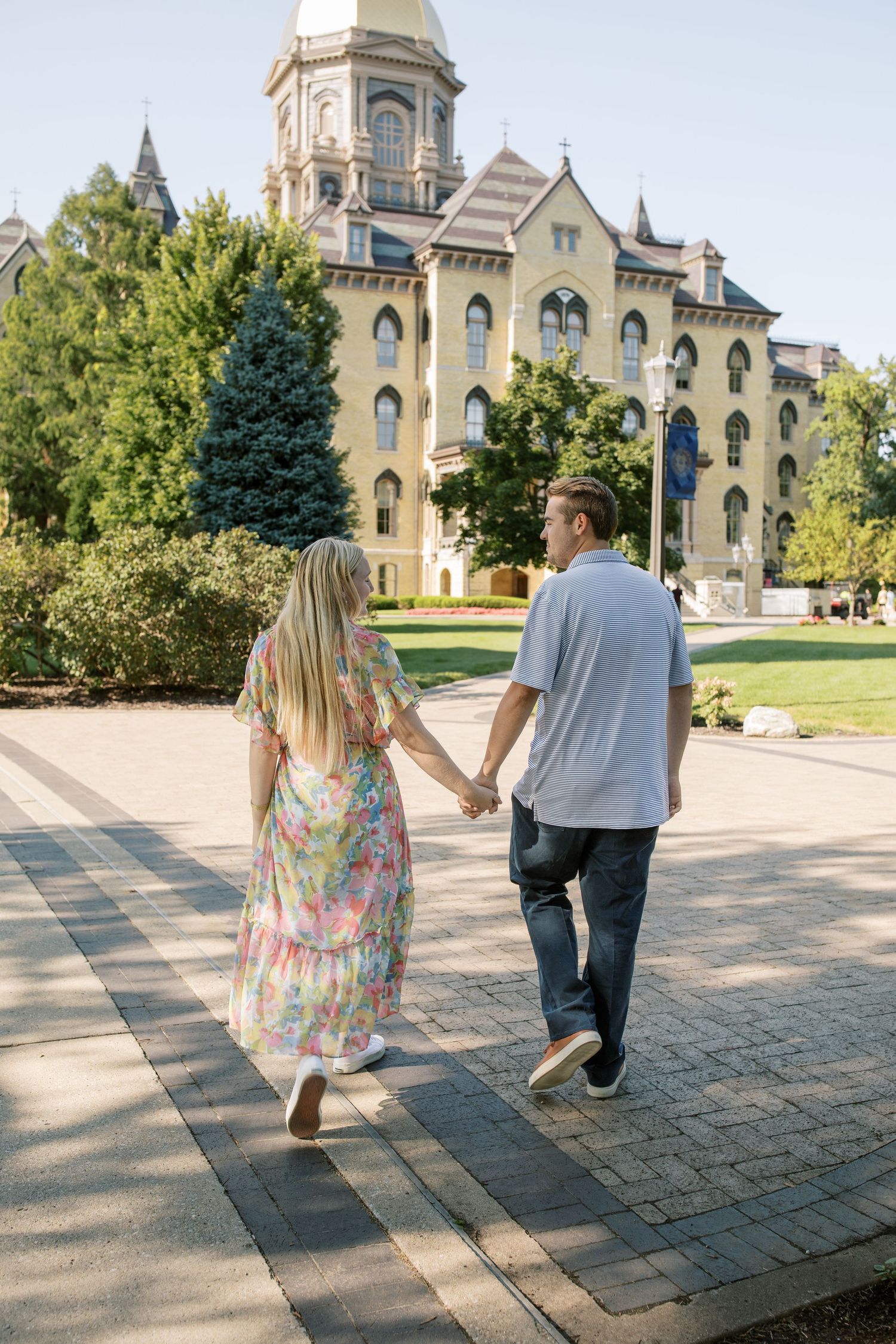A couple walking hand in hand towards the iconic Notre Dame Main Building.