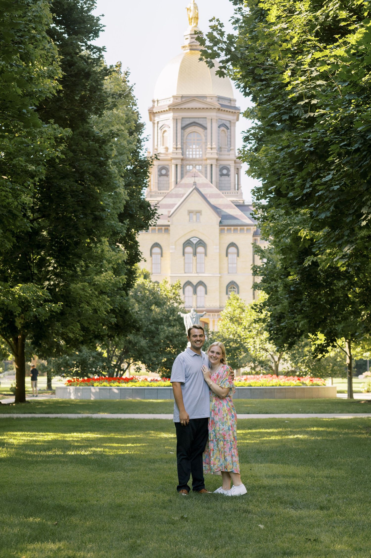 A couple poses on a lawn in front of the iconic Notre Dame golden dome.