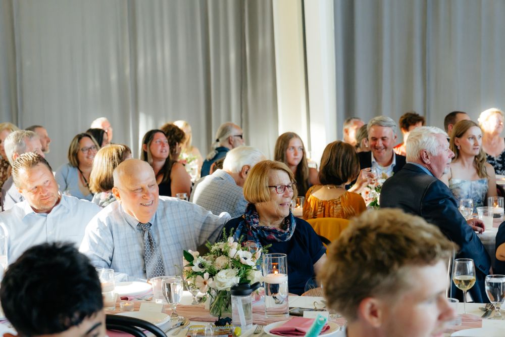 People gathered at round tables for an event with floral centerpieces and white curtains in the background.
