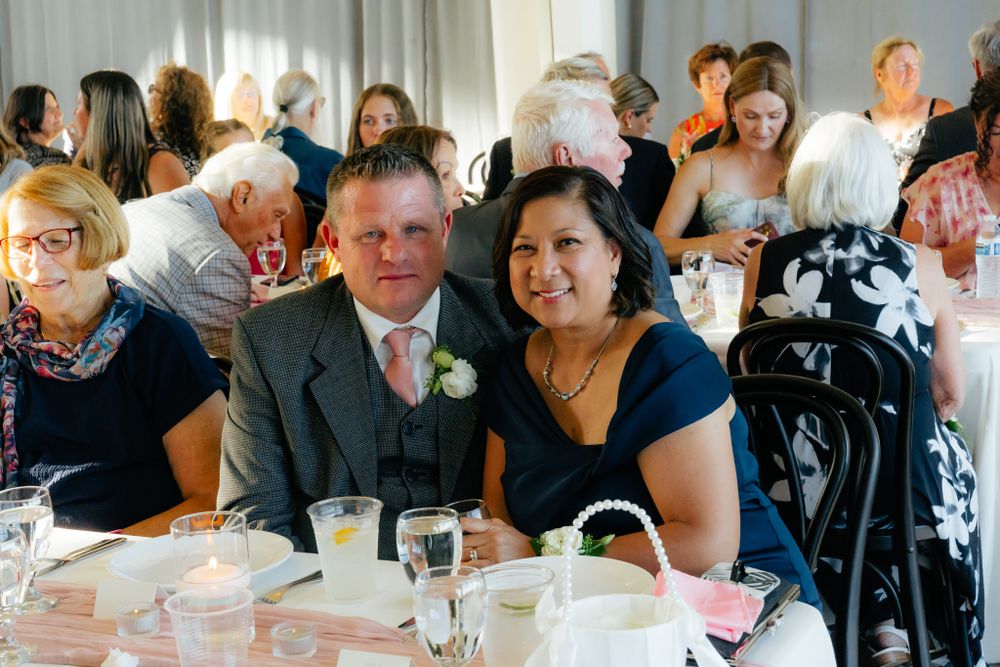 Wedding reception guests seated at round tables in a bright, elegant dining room.