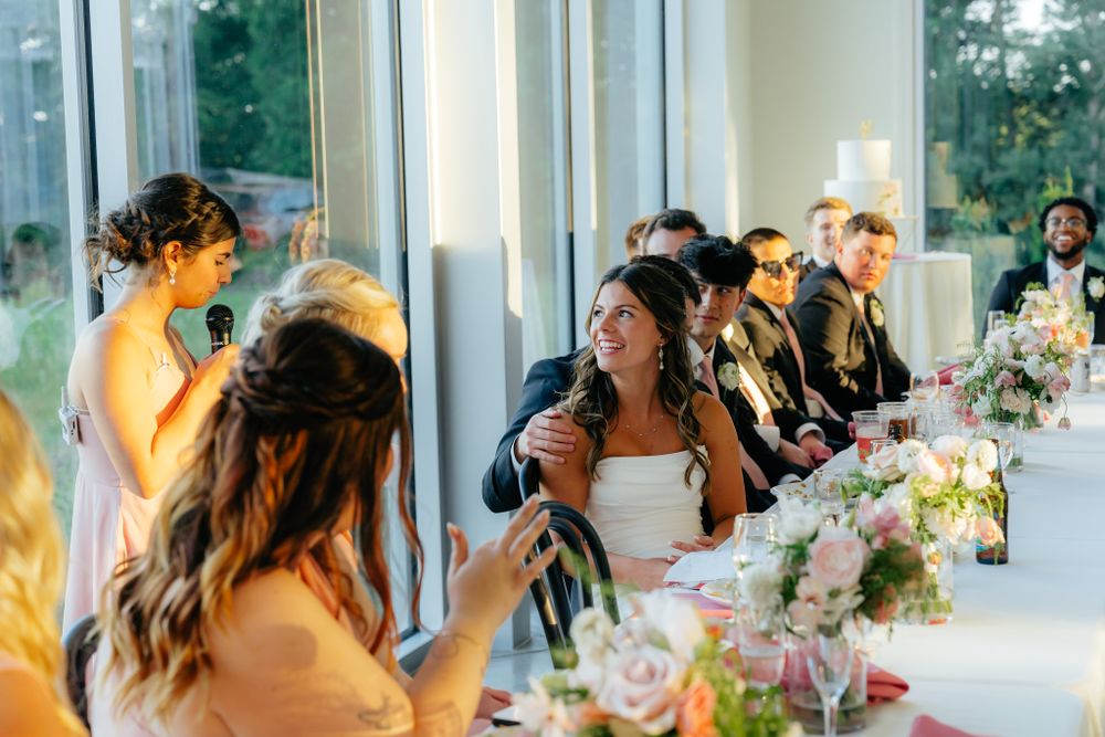 Wedding party guests seated at a long table decorated with pink floral centerpieces during an elegant reception.