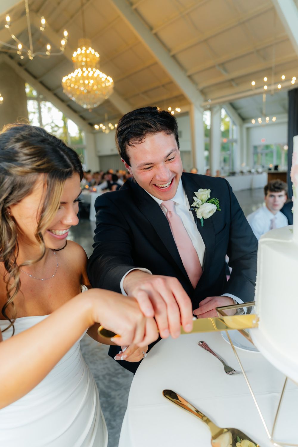 Couple sharing a joyful moment while cutting their wedding cake in an elegant reception hall.