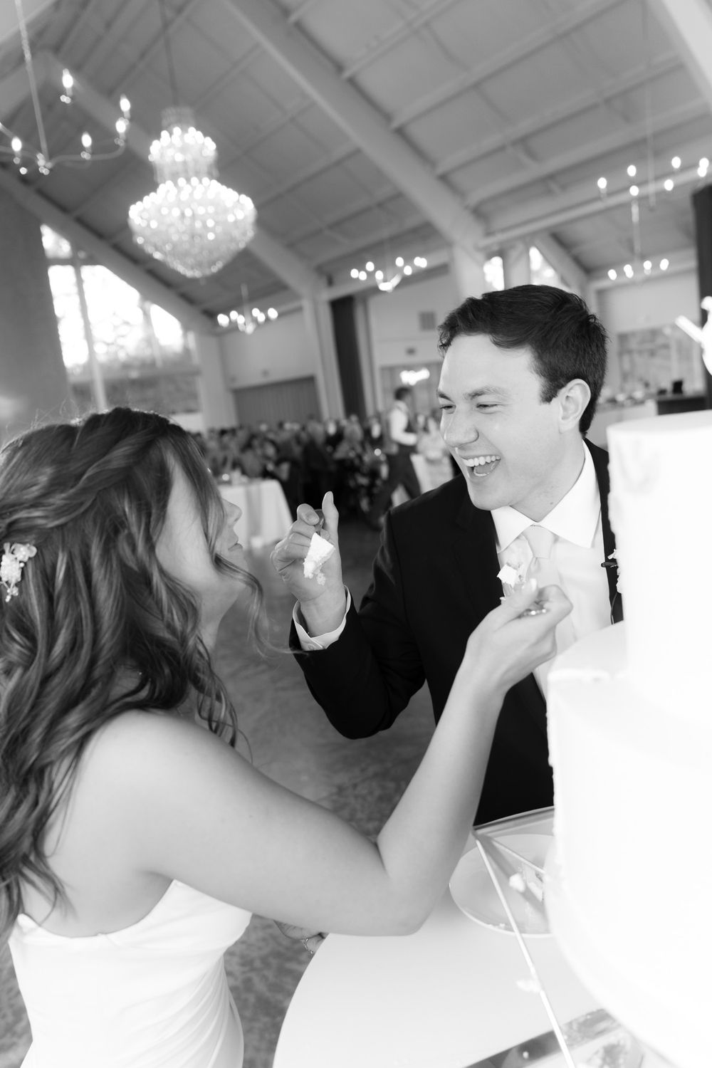 A joyful newlywed couple shares a playful moment feeding each other cake during their wedding reception.