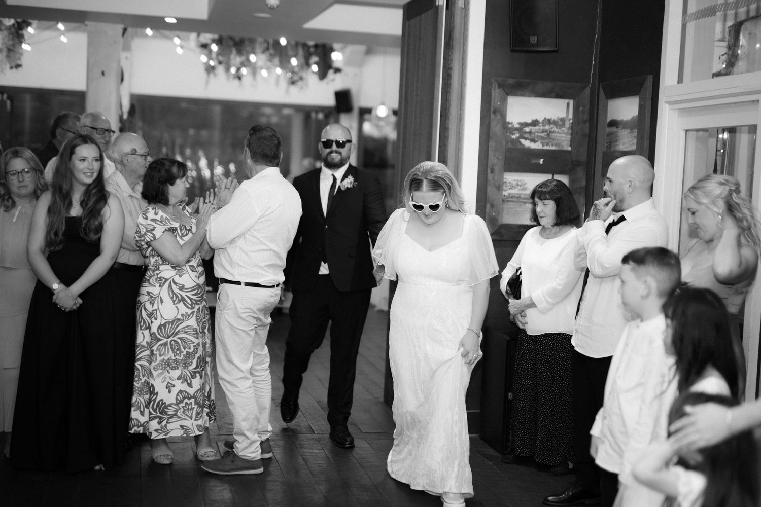 Happy couple in wedding attire share cake while wearing leafy green leis at their reception celebration.