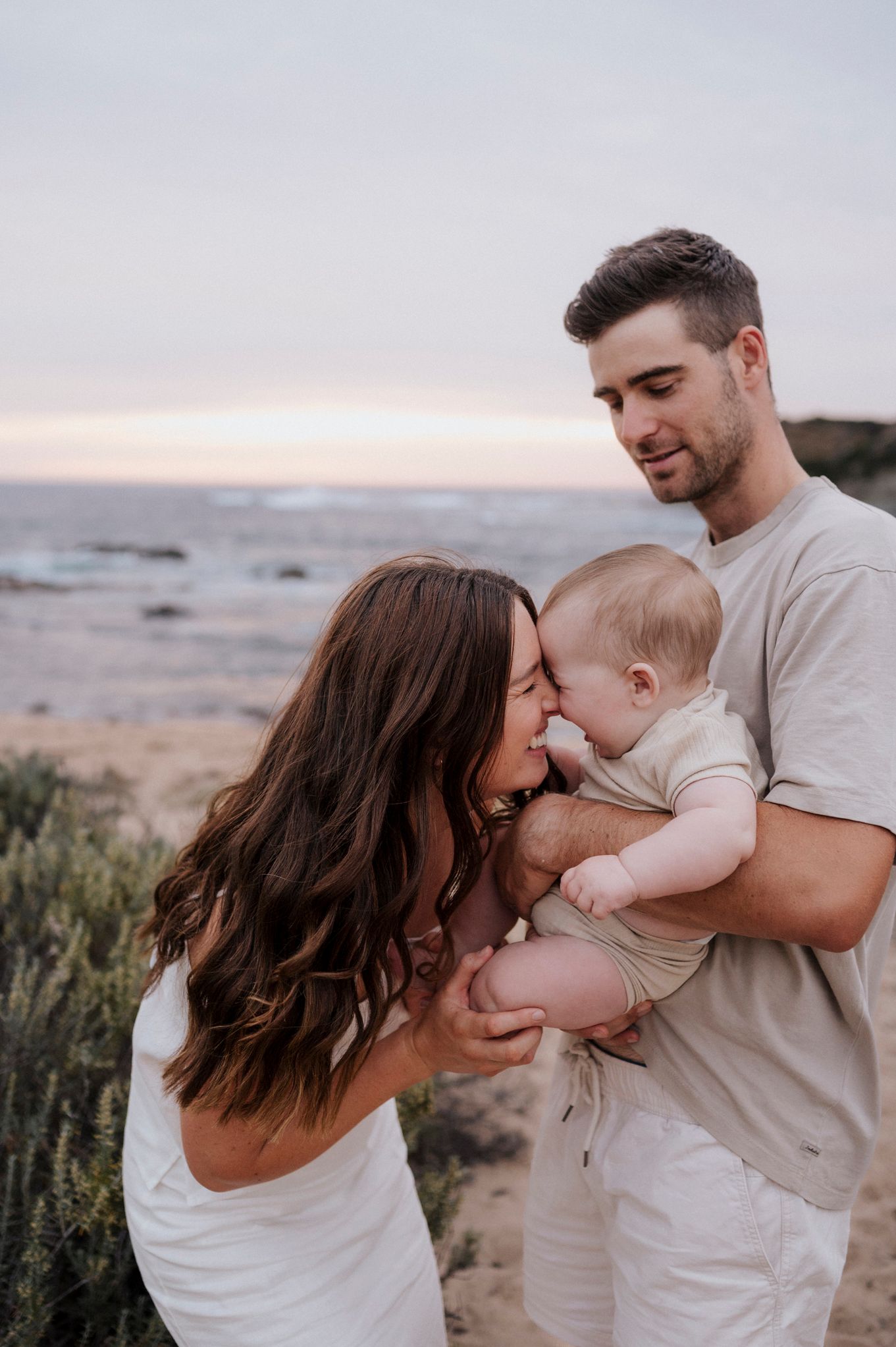 Family shares intimate moment together on coastal cliff at sunset.
