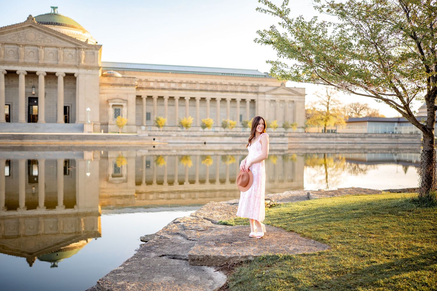 A person in a pink dress stands by the reflection pool at Chicago's Museum of Science and Industry at sunset.