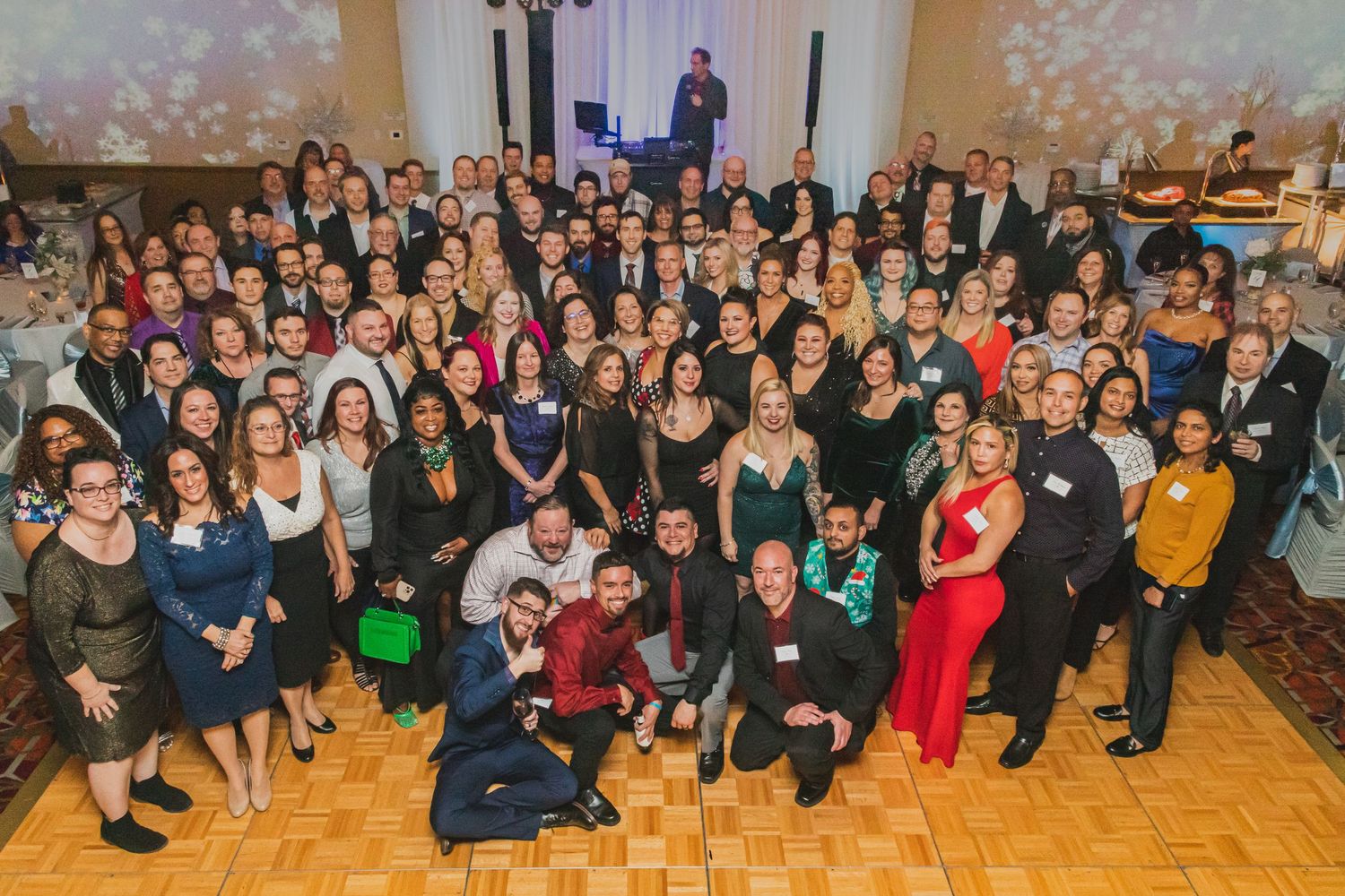 Large group photo of formal event attendees gathered in a ballroom with festive lighting.