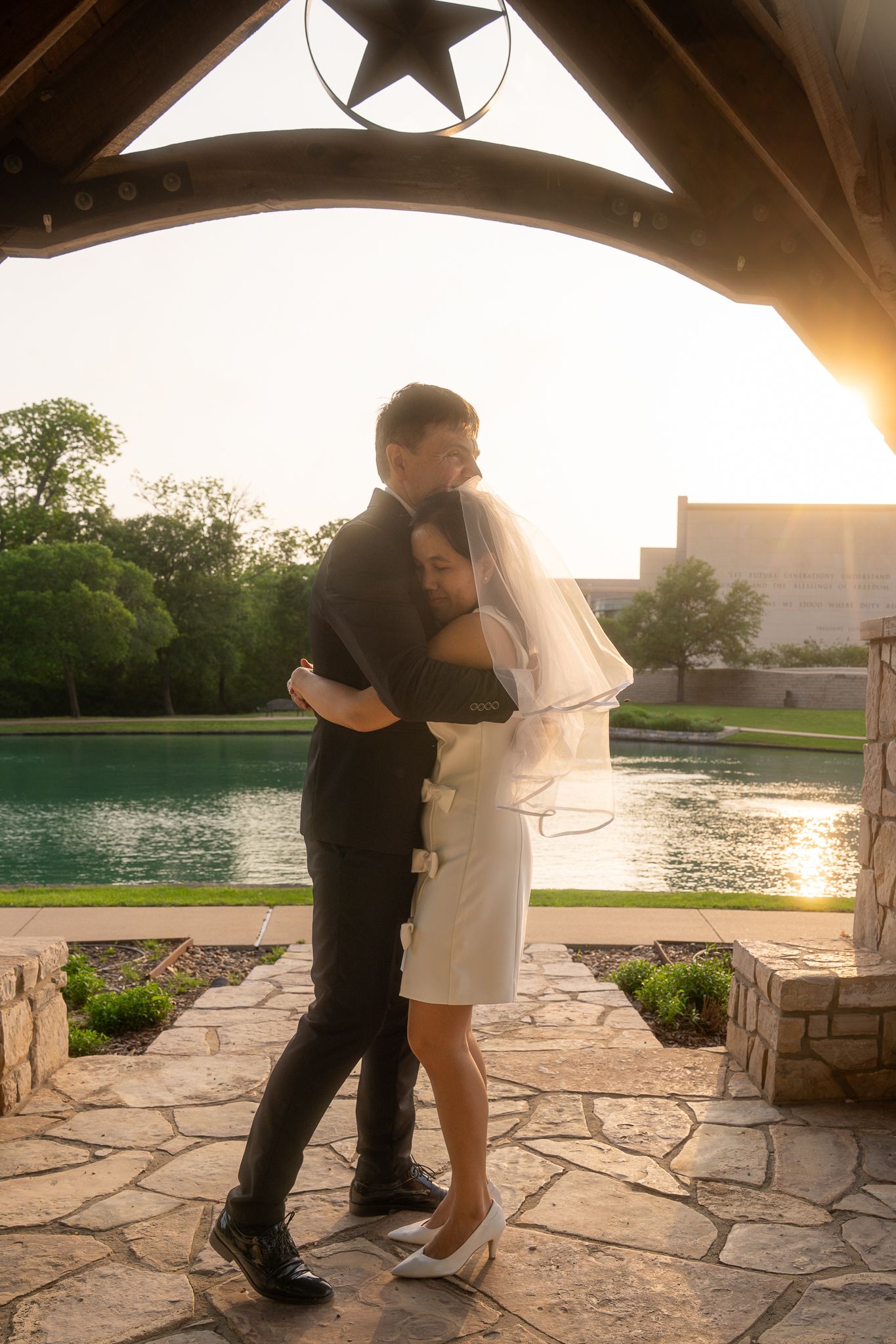 Romantic silhouette of couple embracing on stone patio at sunset with lake and star decoration in background.