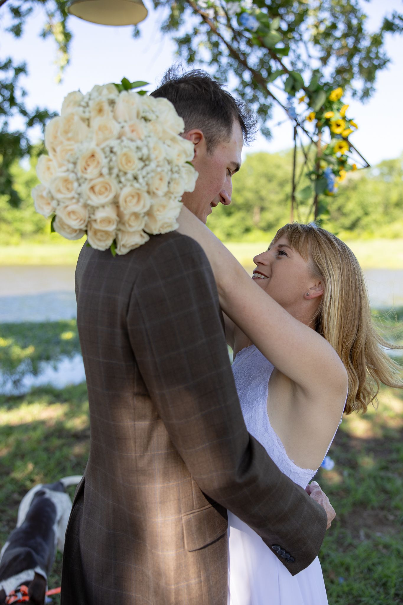 Couple shares an intimate moment at an outdoor wedding ceremony with white rose bouquet and natural scenery.