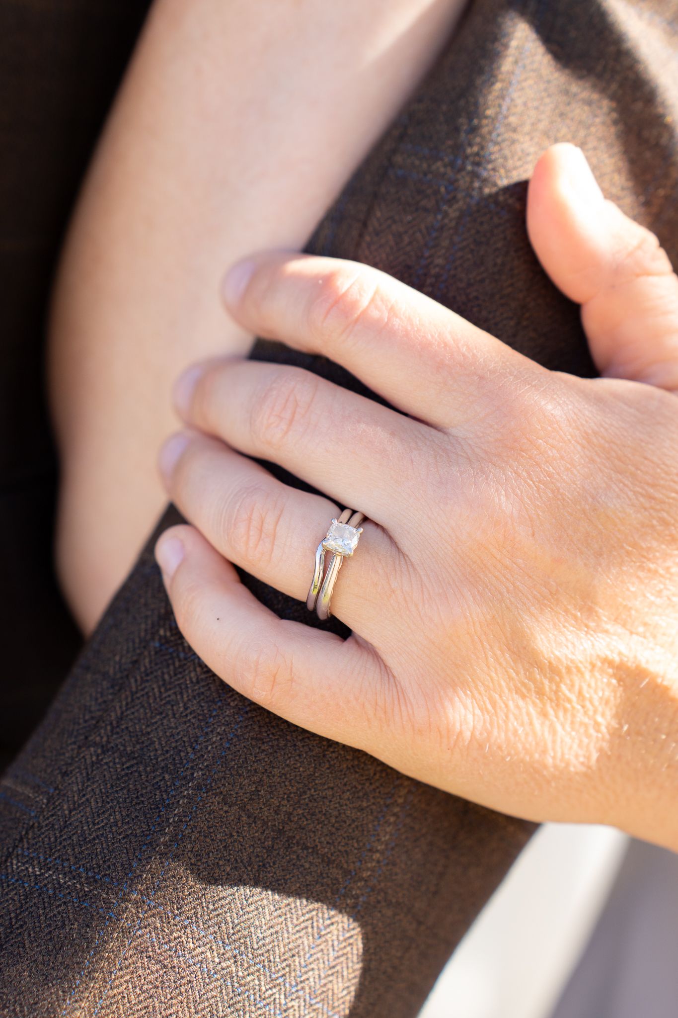 Close-up shot of a hand wearing a silver ring against a dark fabric background in sunlight.