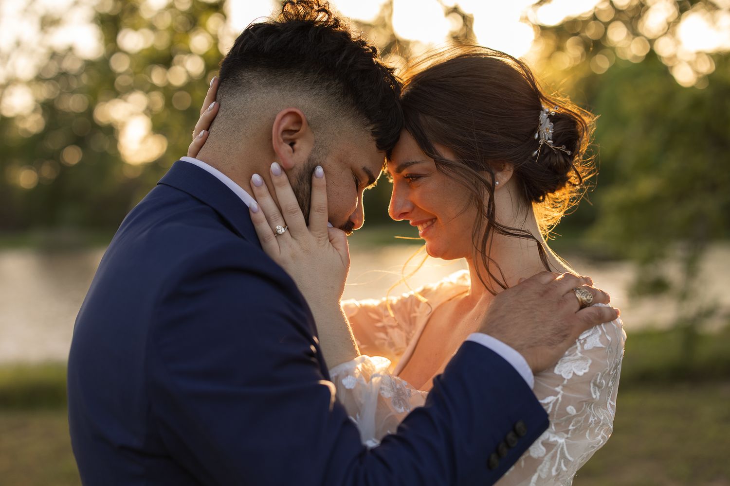 A romantic wedding couple embraces in a tender moment at sunset with golden light glowing behind them.