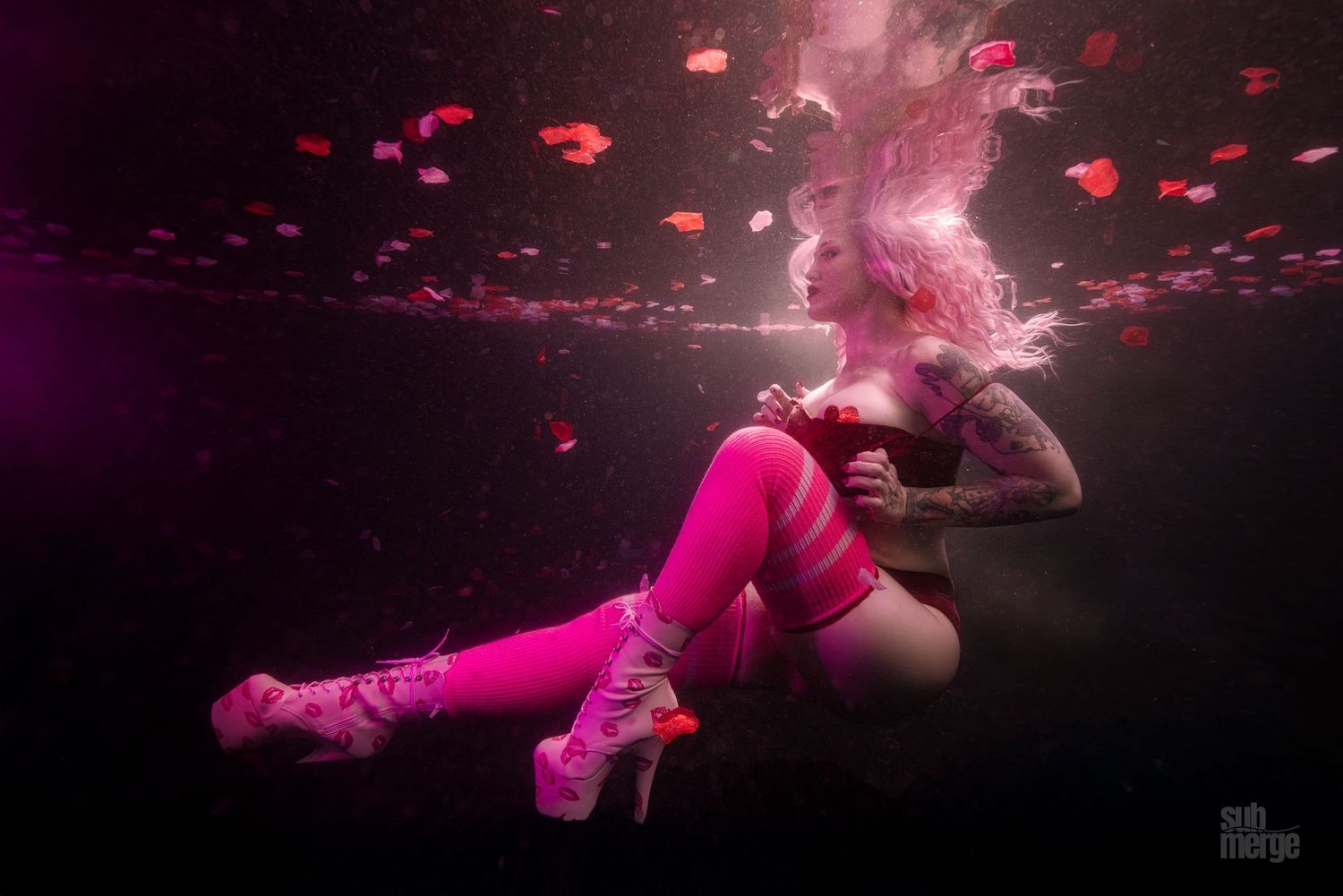 A figure in bright pink clothing floating underwater with pink and red bubbles creating a dreamy underwater scene.