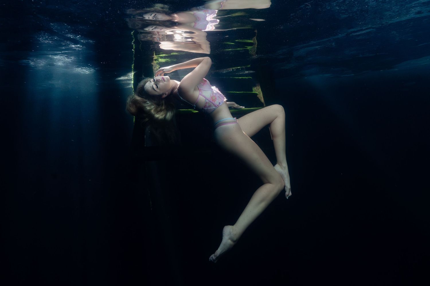 Figure floating gracefully in dark underwater scene with beams of blue light filtering from above.
