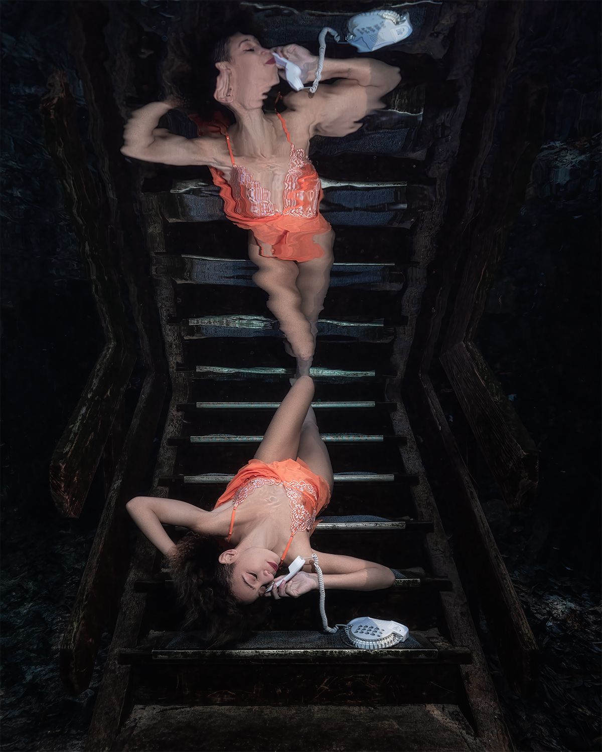 Two dancers in coral leotards pose dramatically on wooden stairs in a dark atmospheric setting.