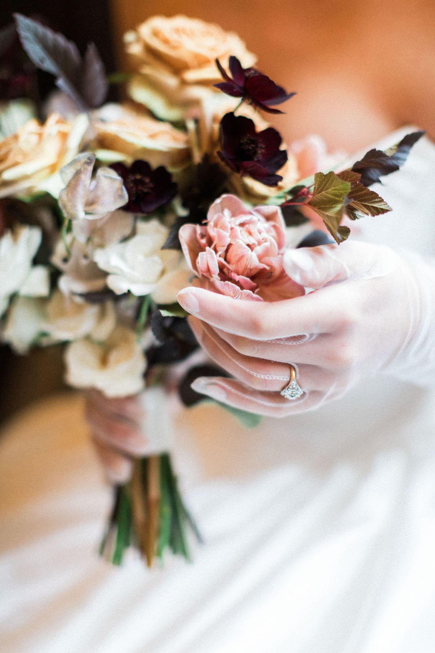 A close-up of a bride's hand holding a wedding bouquet with pink and peach roses featuring an engagement ring detail Oxford Bodelian Library