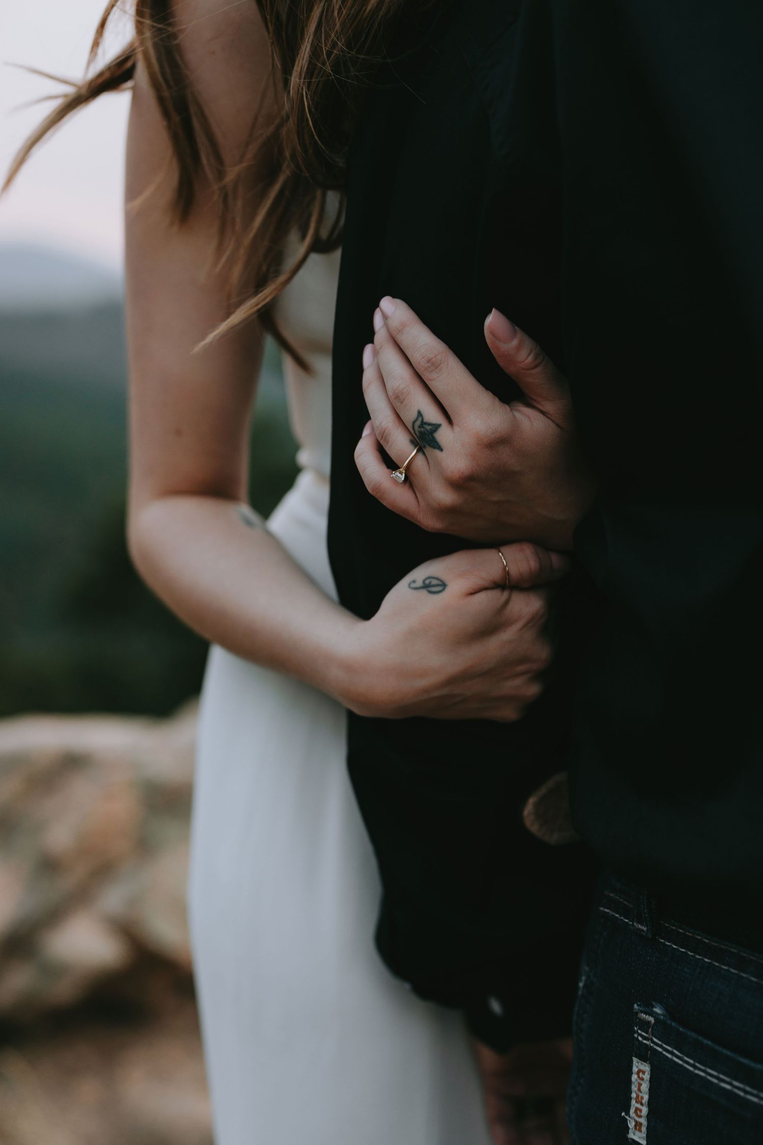 An intimate couple embraces in golden sunlight against a forest backdrop.