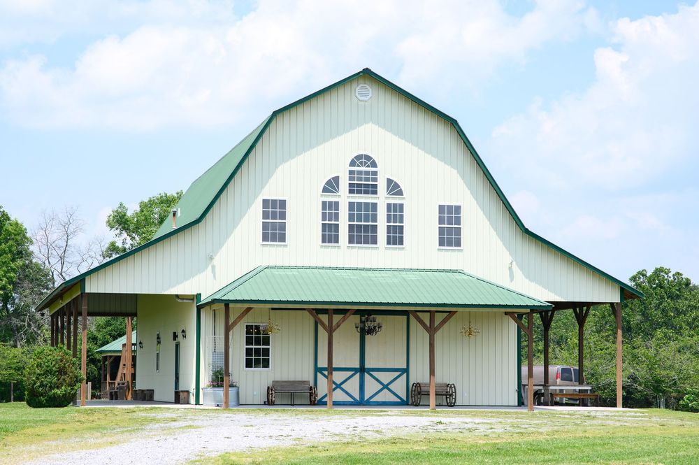 White and mint green barn-style building with gambrel roof and arched window features stands against blue sky.