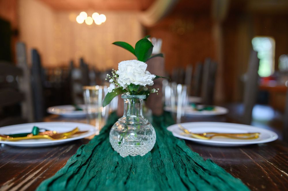 Green and gold wedding table settings with elegant floral centerpieces at an indoor reception venue.