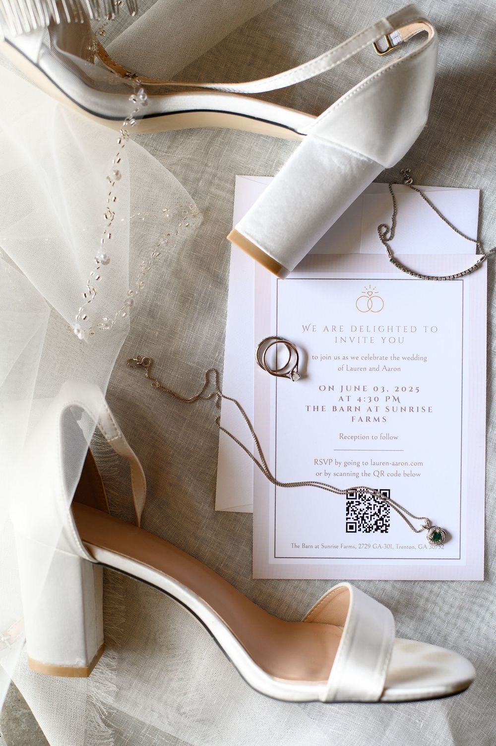 Elegant white wedding shoes with block heels displayed next to invitation card with rings and veil on light linen fabric.