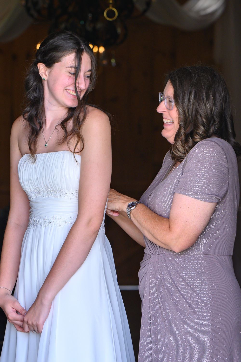 Two people share a joyful moment, with one wearing a white dress and another in a purple dress at an indoor event.