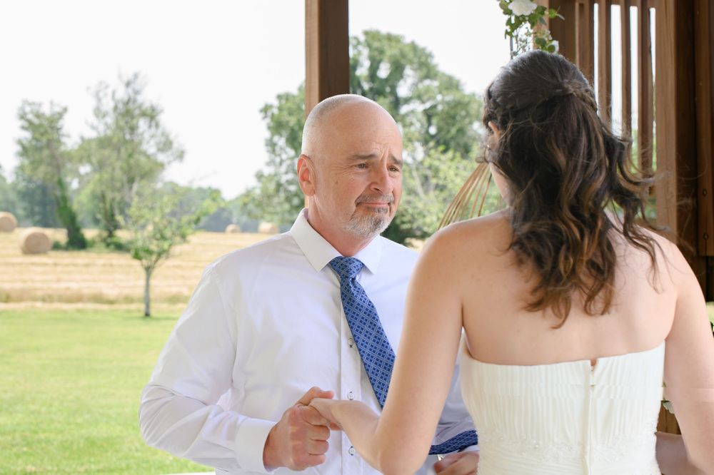 A couple in wedding attire shares a candid dancing moment outdoors at a garden reception surrounded by trees.