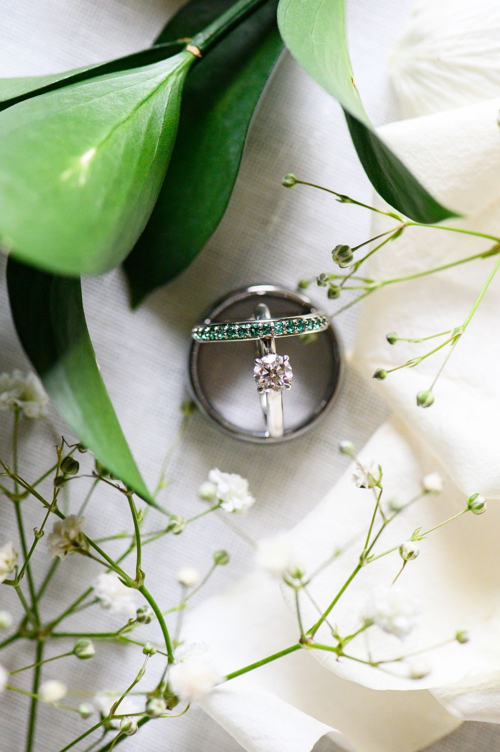 Wedding rings artistically photographed among delicate baby's breath flowers and green leaves on white background.
