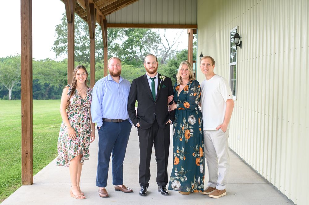 Wedding party members standing in a covered walkway outside a white building with green surroundings.