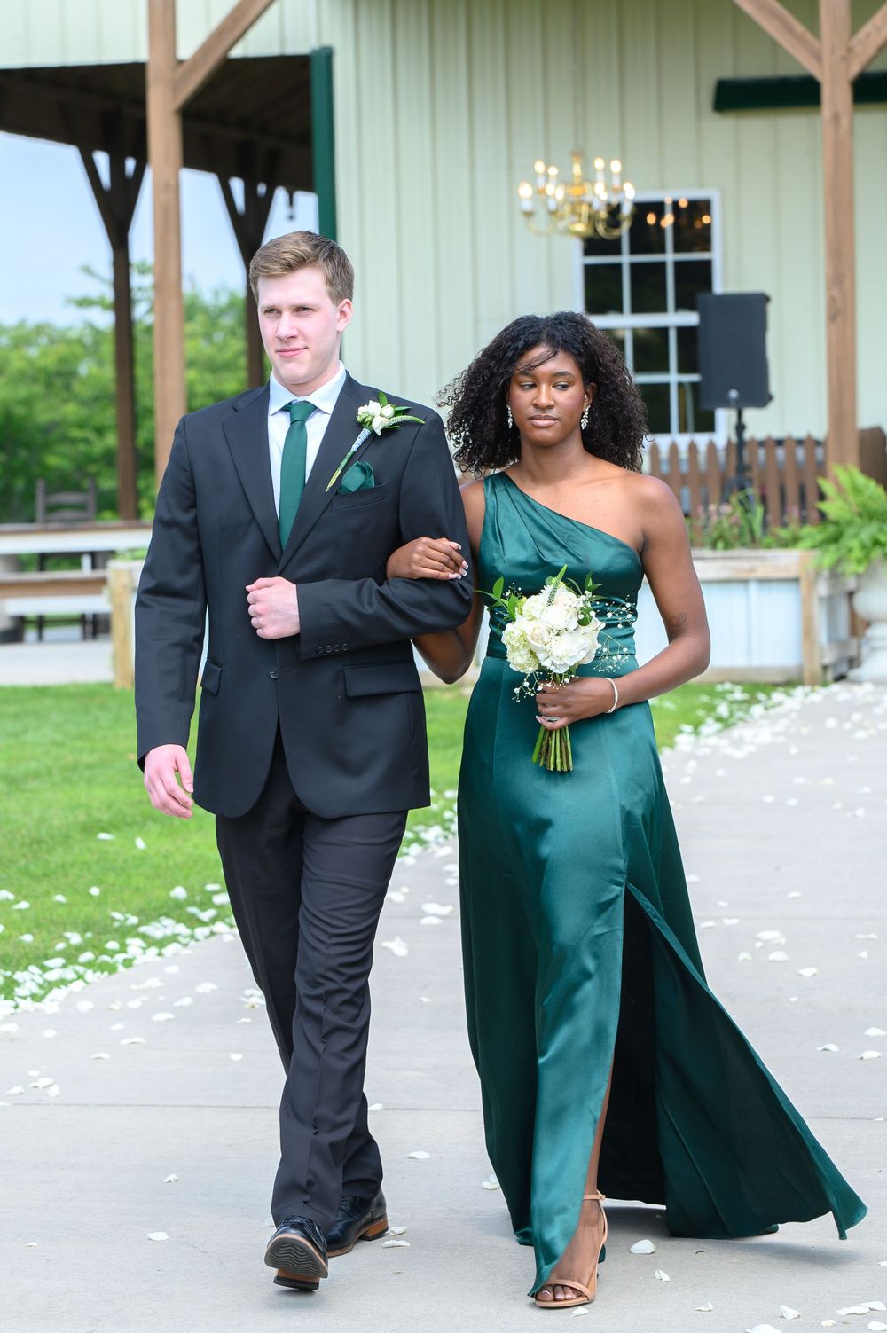 A couple in formal attire walking outdoors, wearing emerald green and black for a wedding ceremony.