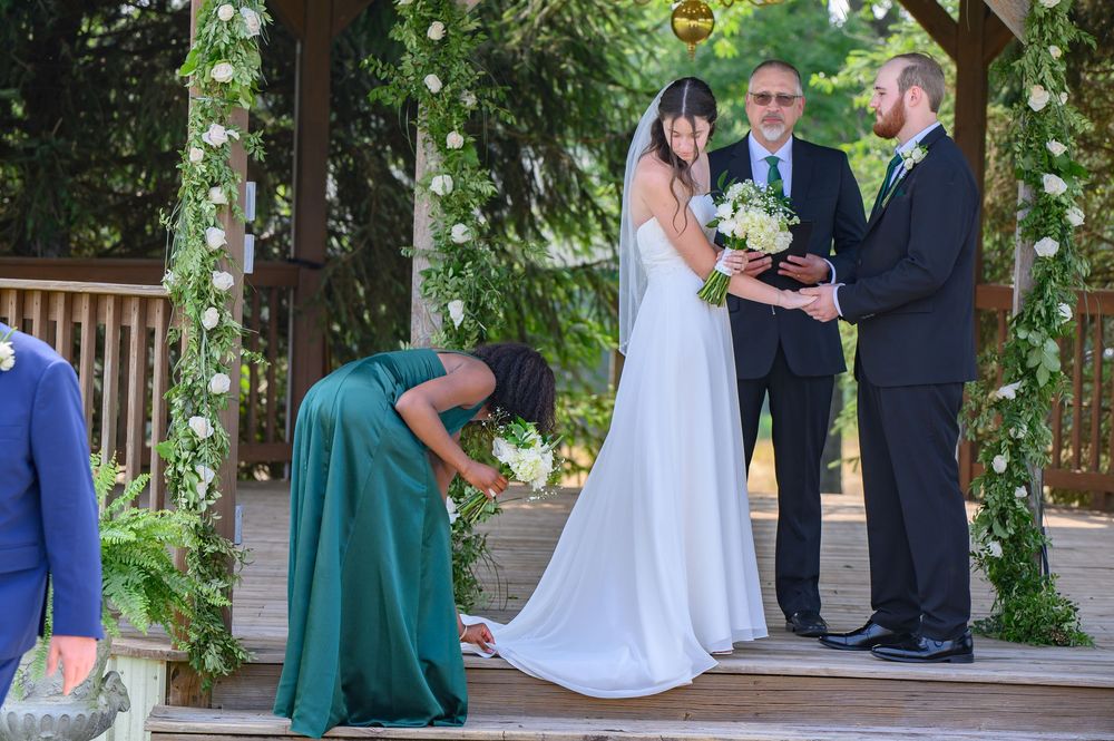 An outdoor wedding ceremony takes place on a wooden deck surrounded by lush greenery and forest trees.