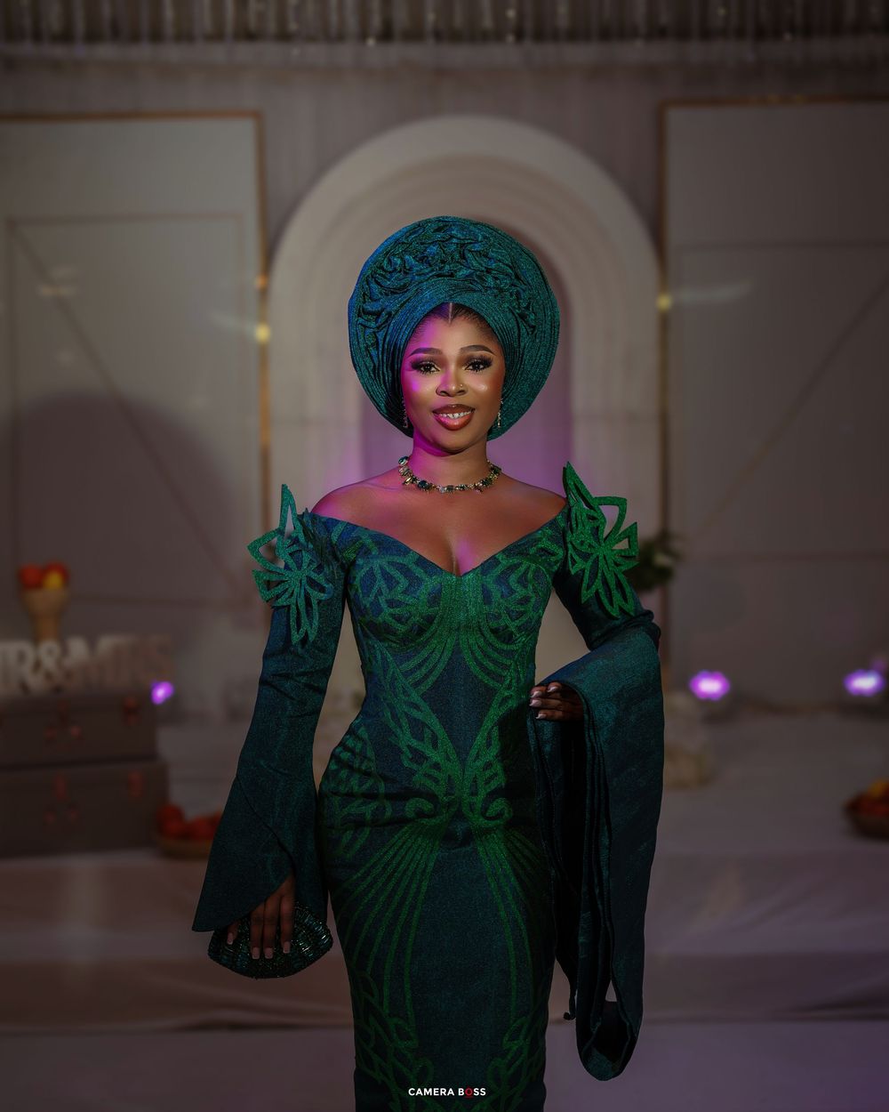 An elegant emerald green evening gown with an ornate headpiece and jeweled neckline glows under purple stage lighting.
