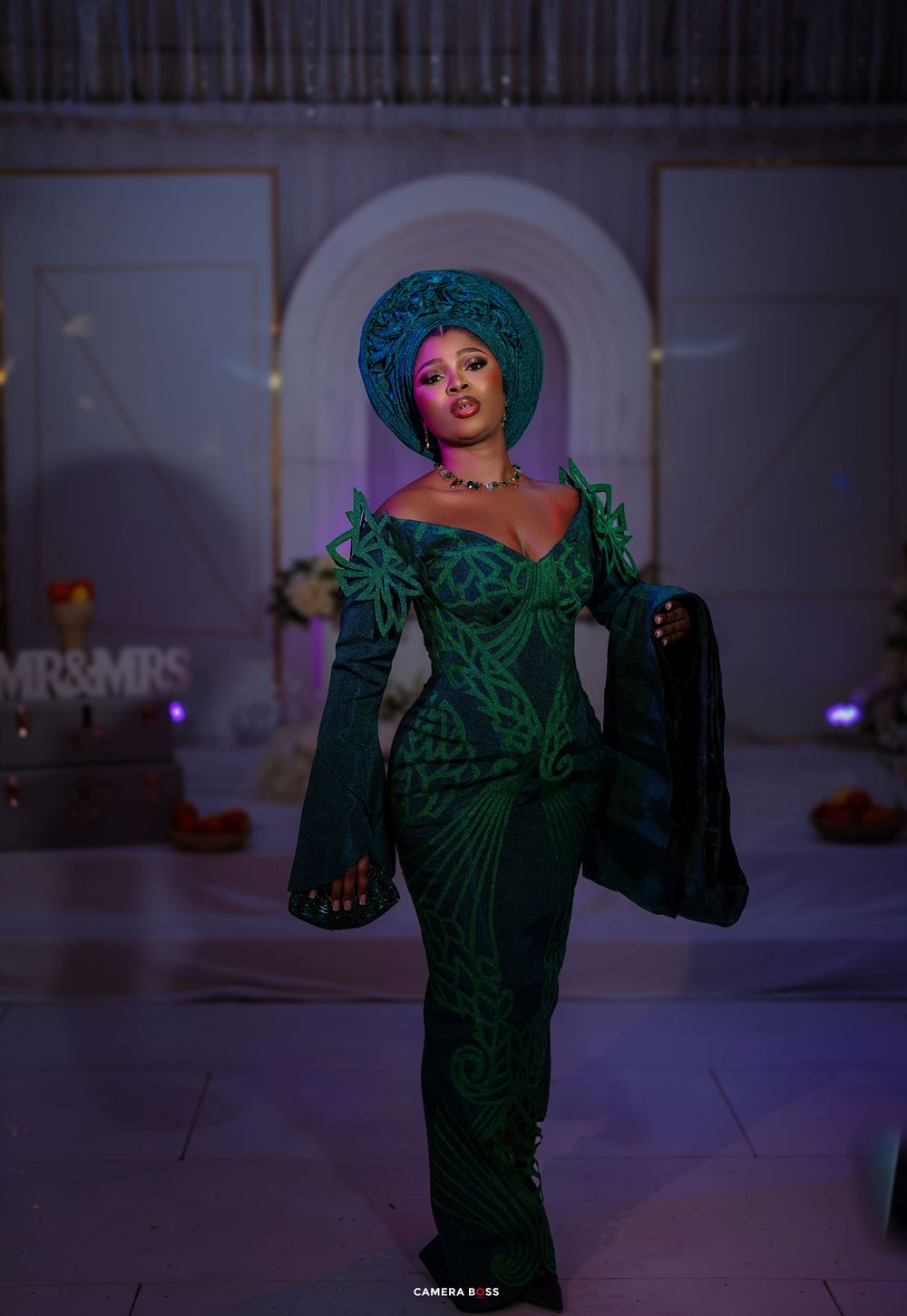 A stunning emerald green formal gown with dramatic bell sleeves and intricate patterns glows under atmospheric lighting.