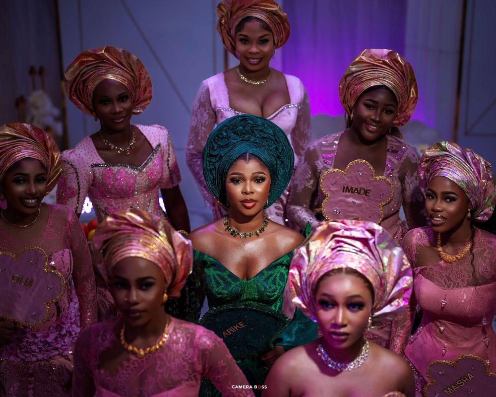 Wedding guests in traditional African attire dance and celebrate during a purple-lit reception party.