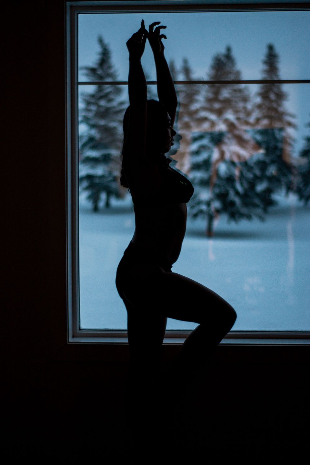 Silhouette of person stretching by window with snowy winter scene outside.