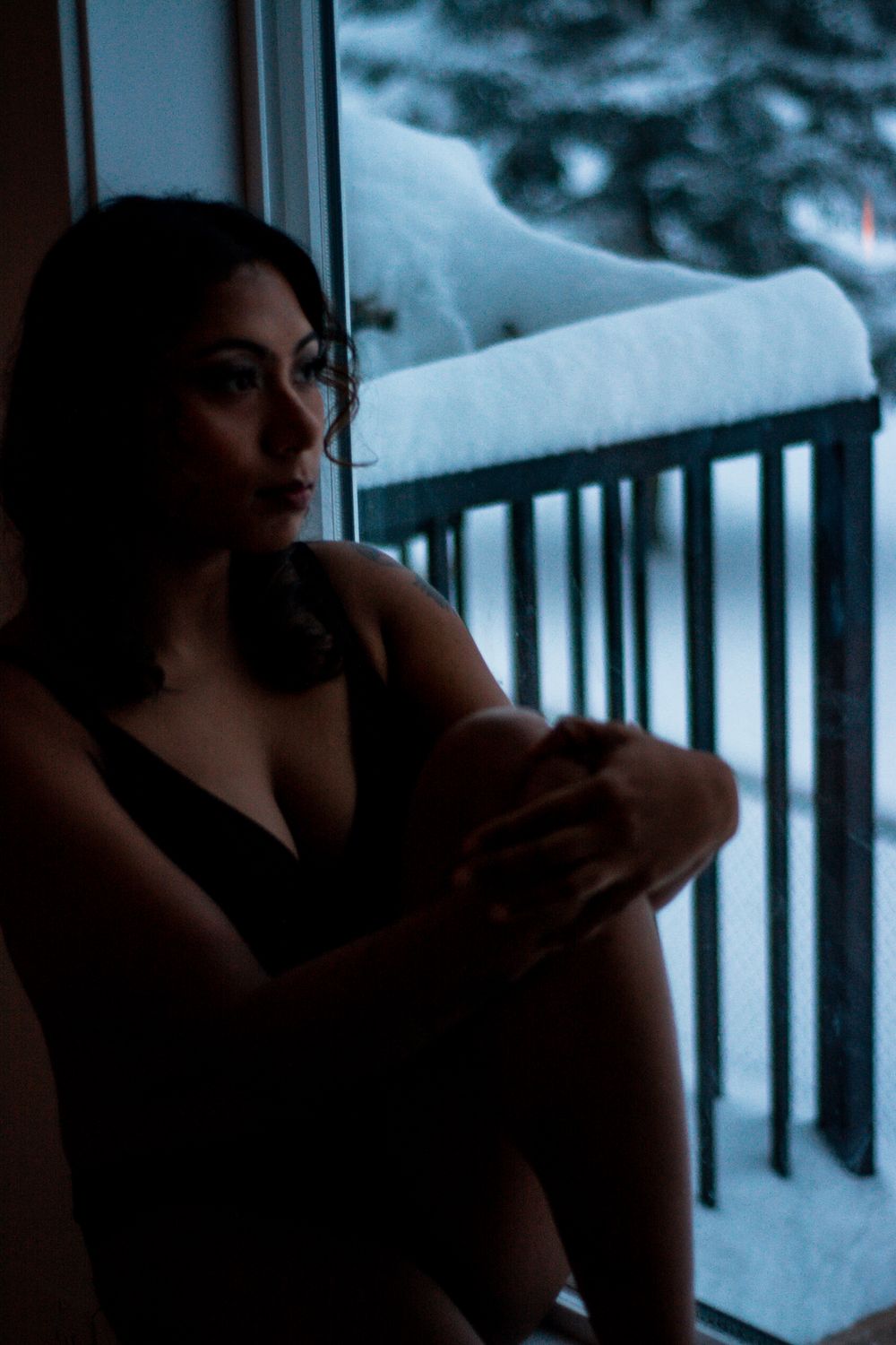 Moody winter portrait by window overlooking snow-covered balcony.