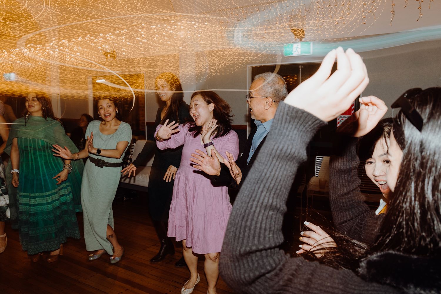 Wedding guests dancing and celebrating with high energy under decorative string lights.