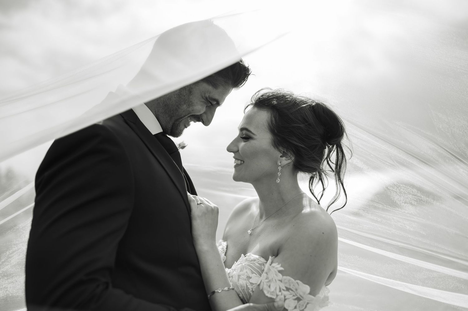 A romantic black and white wedding scene showing silhouettes of a couple in an intimate moment with flowing veil.