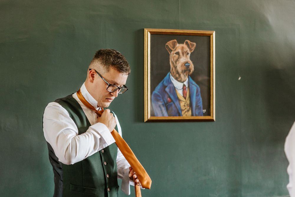 Groomsmen and groom getting ready in front of chalkboard wall with dog portraits.