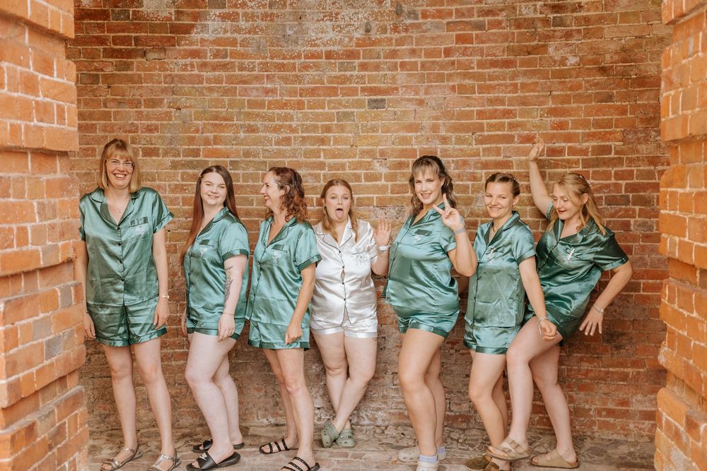 Bridesmaids in teal robes sit together on brick steps during wedding preparations.
