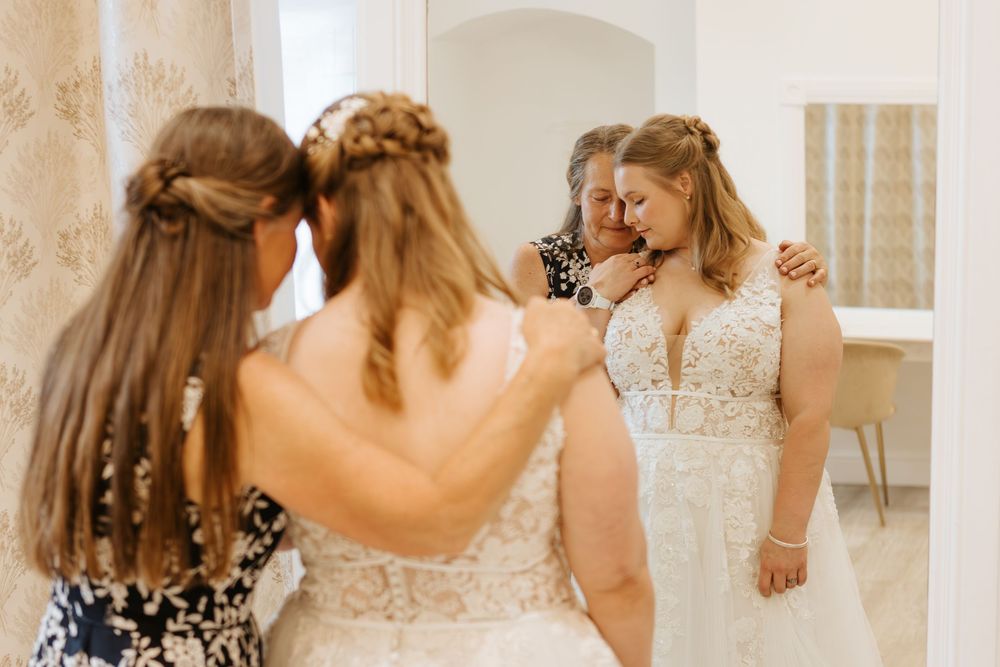 A group in sage green bridesmaid dresses and white wedding gowns gather for a bridal preparation moment.