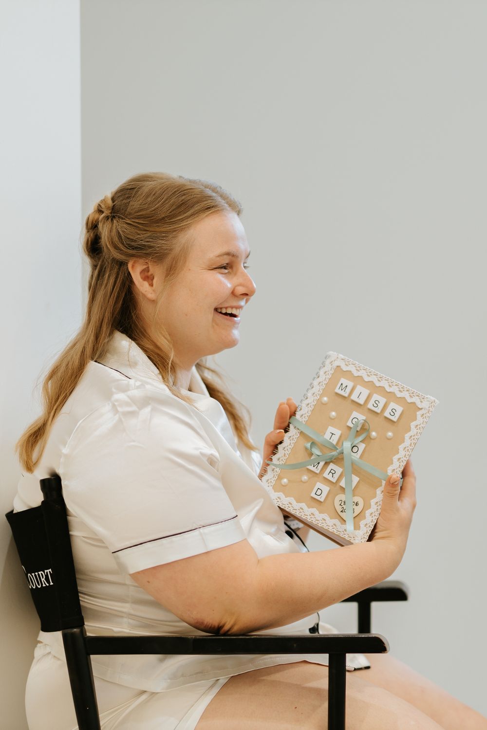 A woman smiles while holding decorative wedding stationery in a bright indoor setting.