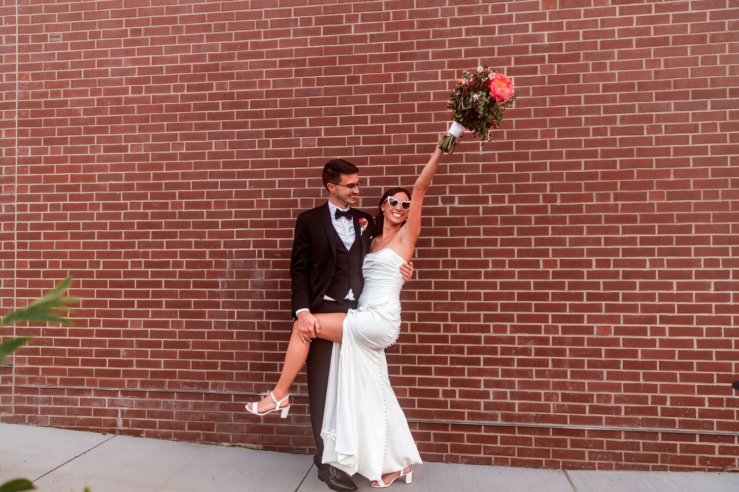 Wedding couple shares a romantic dip pose while dancing against a brick wall backdrop at their celebration.