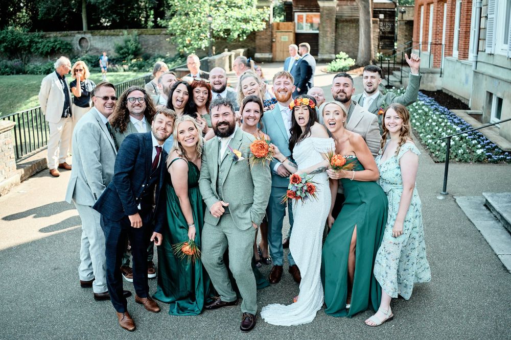 Wedding party dressed in sage green and gray attire posing outdoors at formal celebration.