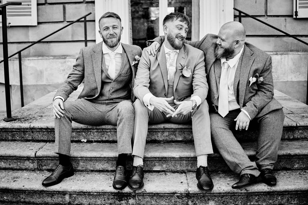 Black and white photo series showing legs and feet of groomsmen sitting on stone steps in formal attire.