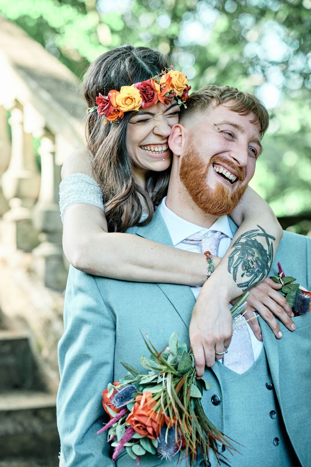 A joyful couple embraces outdoors with a flower crown and bouquet against a bokeh natural background.
