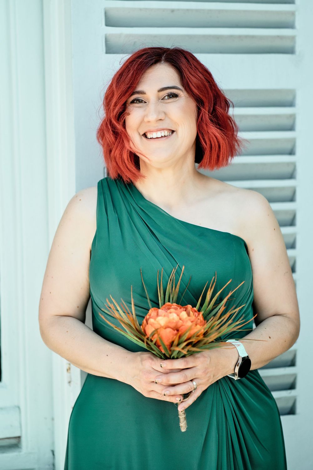 Four connected photos showing a person in an emerald green dress holding orange flowers against a light blue background.