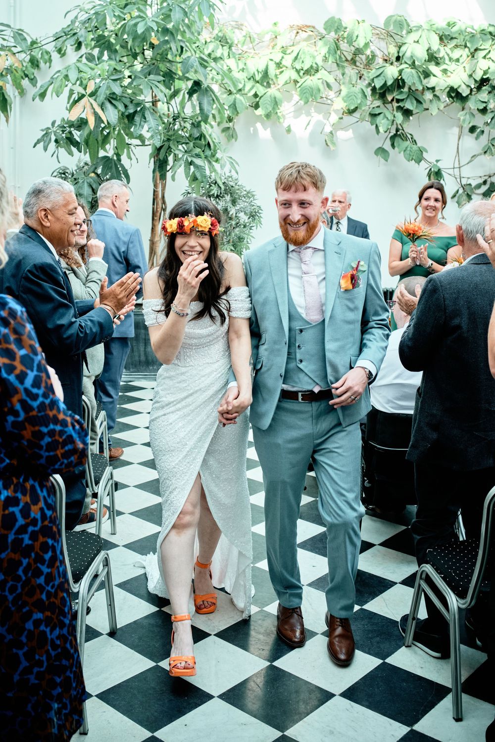 Wedding guests stand and dance on a black and white checkered dance floor at an indoor reception celebration.