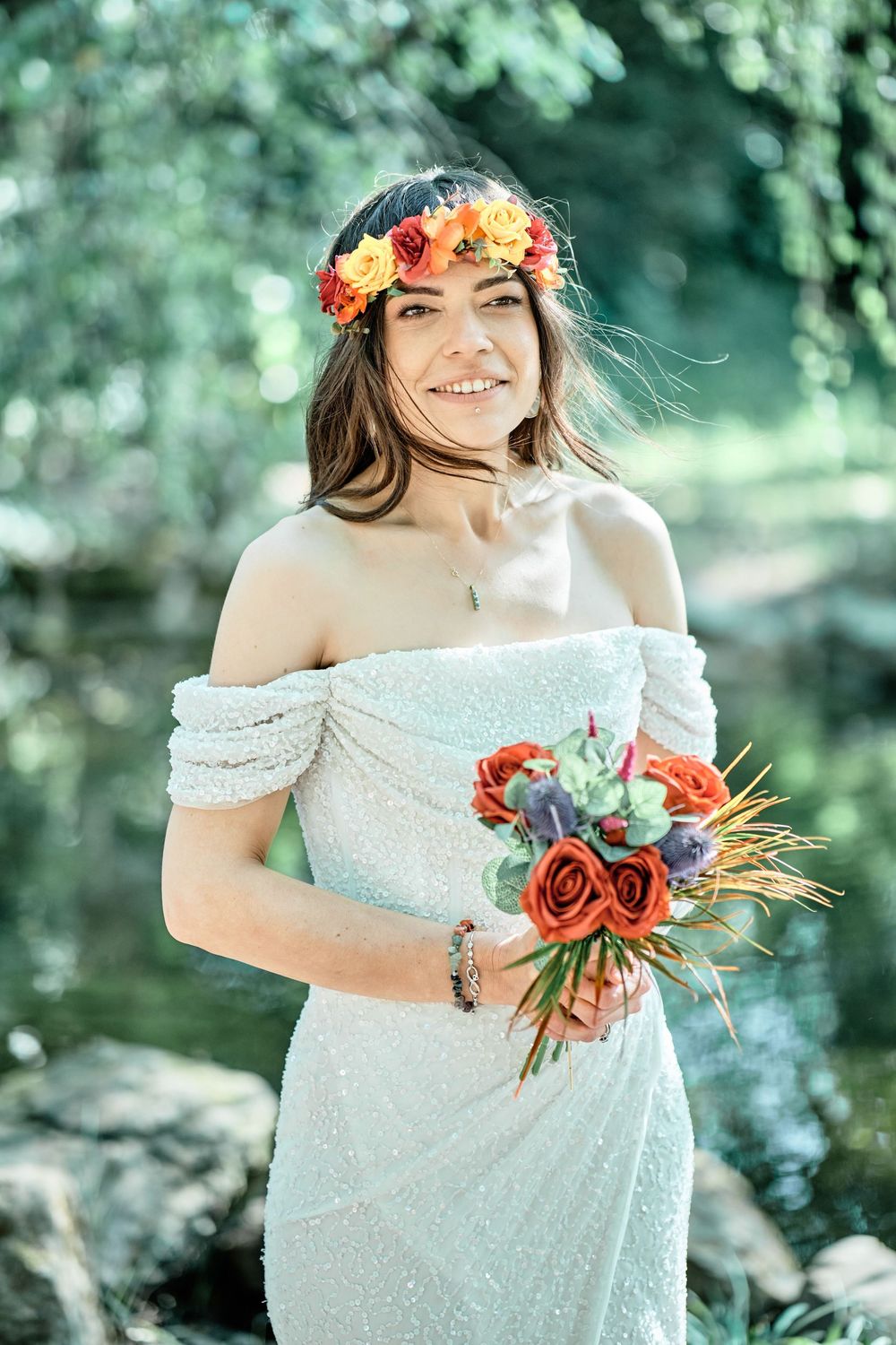 Outdoor maternity photo session featuring an off-shoulder white lace dress and vibrant orange floral crown and bouquet.