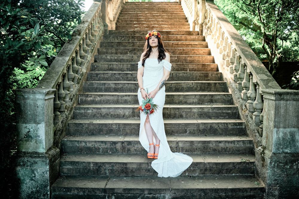 A figure in a flowing white dress stands gracefully on stone garden steps surrounded by lush greenery.