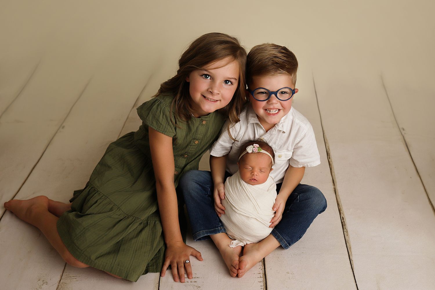 Utah newborn photography. A sweet family portrait with siblings in olive green and white sitting together on a cream-colored floor.