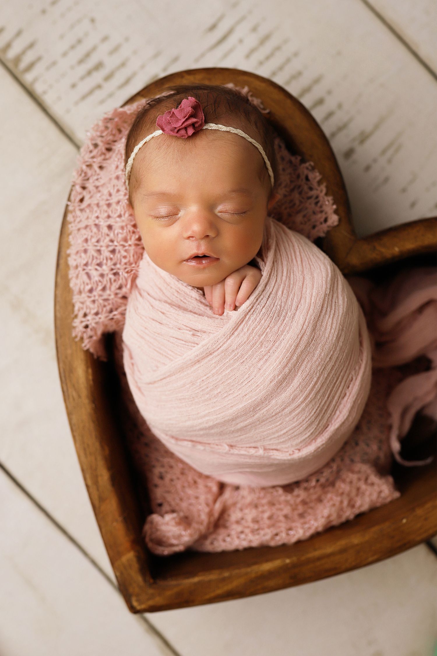 Series of elegant newborn portraits featuring a wooden heart-shaped bowl prop and soft pink wrapping.